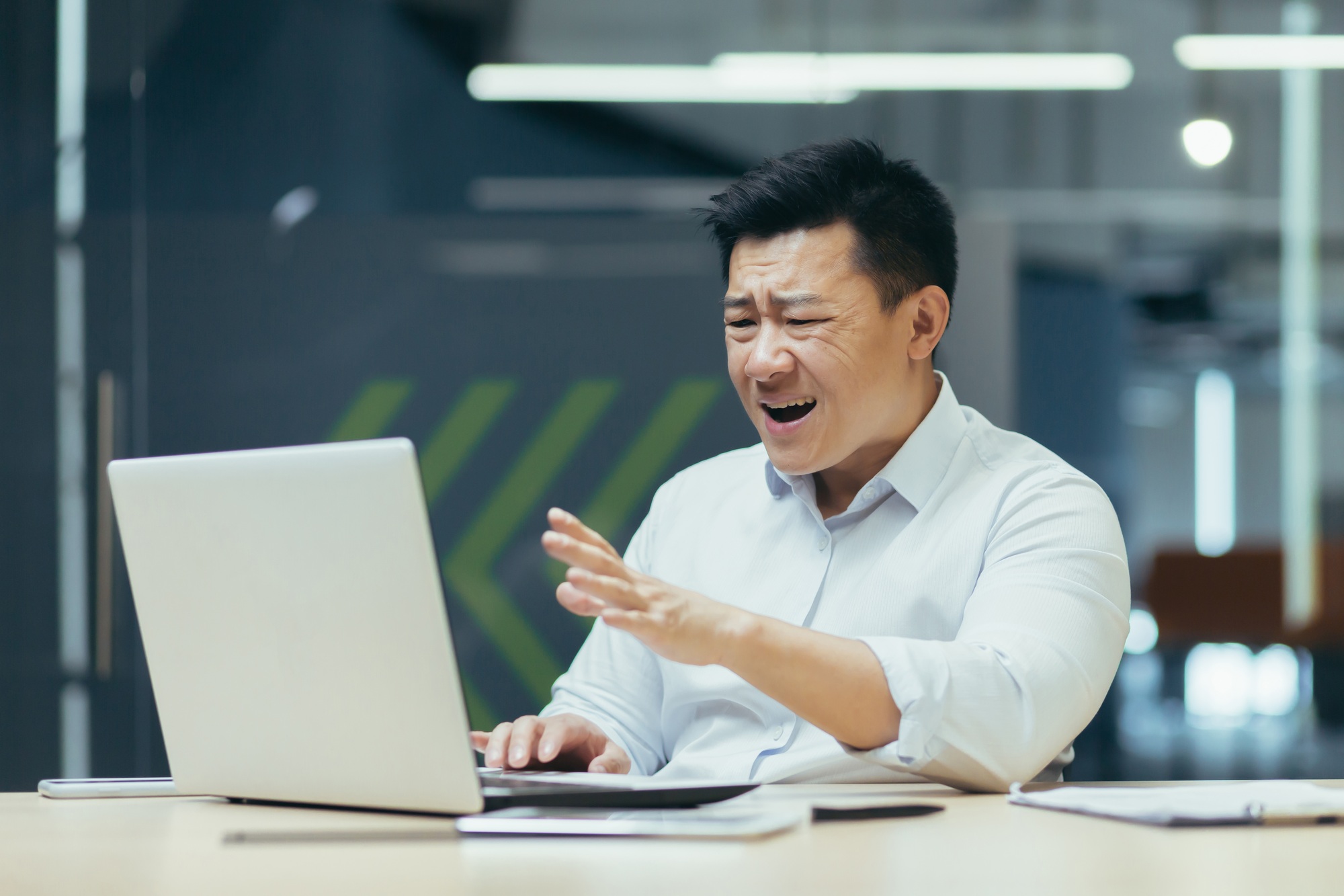 Angry Asian man in the office. Plays online games on a laptop, places bets, lost a bet, lost money